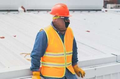 A construction worker wearing PPE gear leaning on a rooftop, showcasing safety at work.