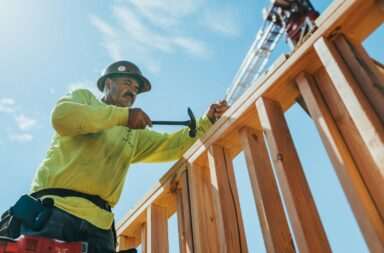 a man in a hard hat and safety gear working on a wooden structure